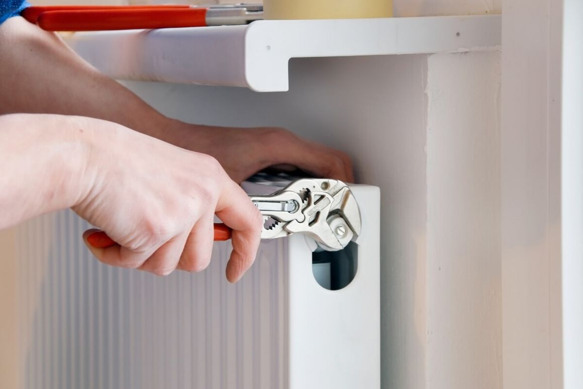 Person montiert Heizkörper mit Zange.